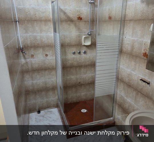 מקלחון זכוכית פינתי מותקן בחדר רחצה מחופה אריחי קרמיקה